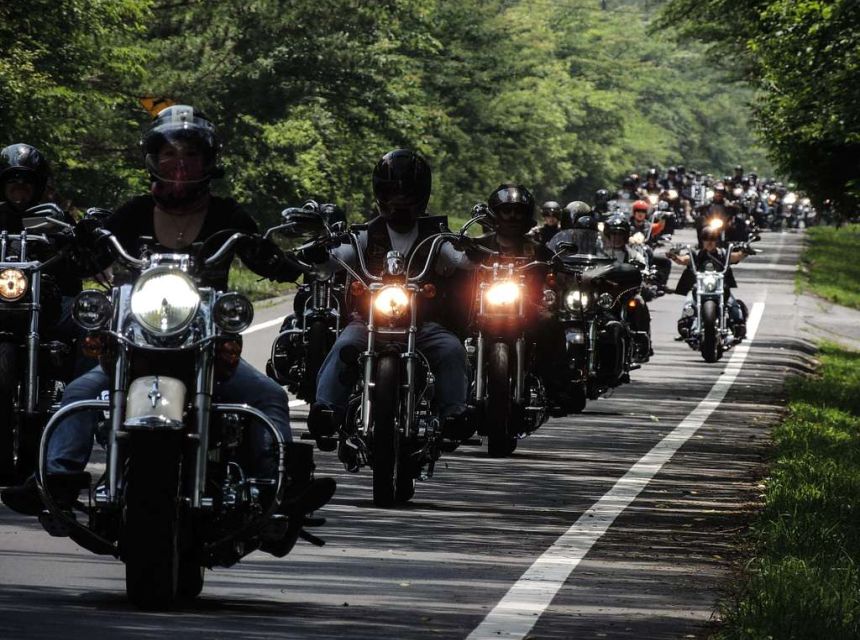 Motorcyclist riding in a line along a two-lane asphalt road.